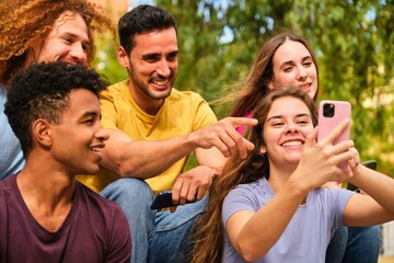 Group of young teenagers watching something funny on mobile phone screen at street.