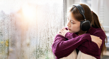 Depressed young woman with headphone sitting near window at home, closeup