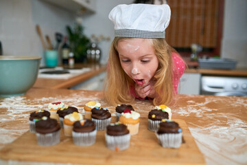 Excited, child and baking cupcake in kitchen on table with hungry girl with wow face in home....