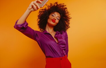Naklejka premium Stylish Woman in Bold Colors Taking a Selfie on Vibrant Orange Background