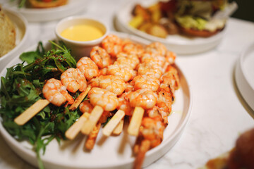 A plate of shrimp skewers with lettuce and sauce, a delicious seafood dish presented on a table with elegant tableware
