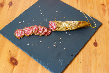 Salami sausages with spices on black slate board on a wooden table. Top view