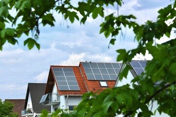 Solaranlage auf Einfamilienhaus umgeben von Blättern symbolisiert die grüne, nachhaltige...