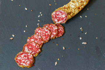 Salami sausage with spices on black slate board. Top view