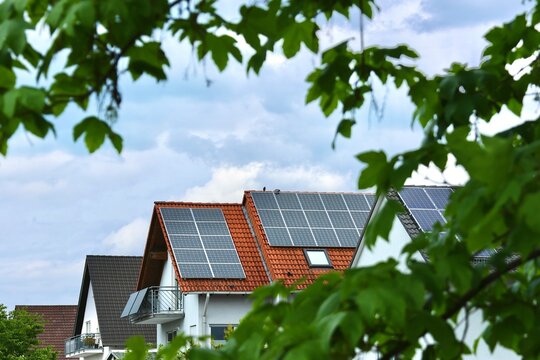 Solaranlage auf Einfamilienhaus umgeben von Bl&auml;ttern symbolisiert die gr&uuml;ne, nachhaltige Stromerzeugung und Energiewende mit Solarstrom zur Nutzung der Sonnenenergie