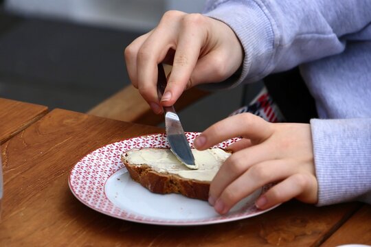 Kind schmiert Brot mit Butter. Frau schmiert ein Butterbrot mit dem Messer