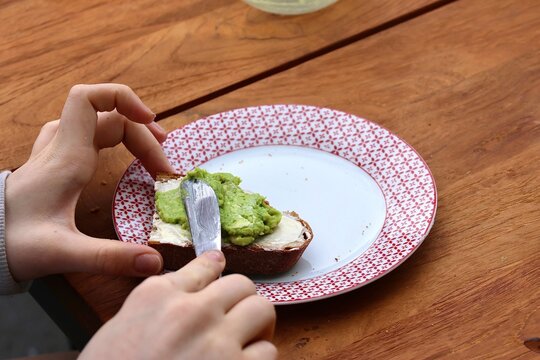 Frau schmiert ein Brot mit gesundem Avocado Aufstrich und Butter mit dem Messer am Esstisch Close up (Konzept gesunde Fette zur low-carb Di&auml;t)