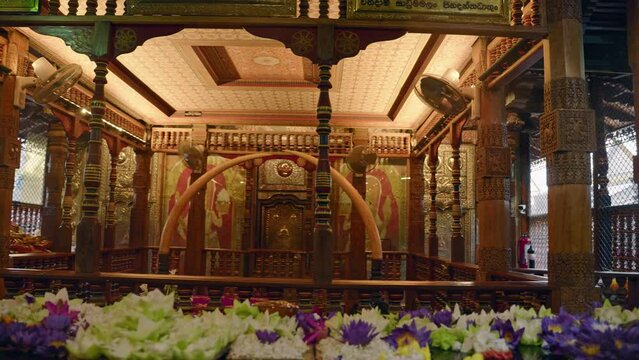 Interior view of Sri Dalada Maligawa, Kandy with ornate wood carvings, sacred Buddha Tooth relic behind gold gate. Worshippers, tourists visit heritage site, experience religious ceremonies, culture.
