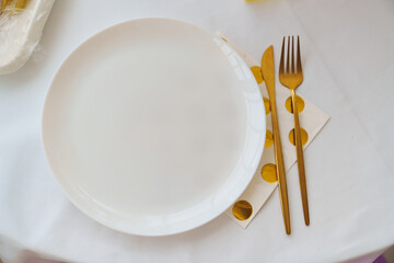 Table setting. White round plate with golden fork, knife and napkin.