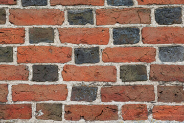 Close-up of a fragment of the wall of an ancient red brick building. There are chips and cracks, and a pattern of black brick ends. Background. Texture.