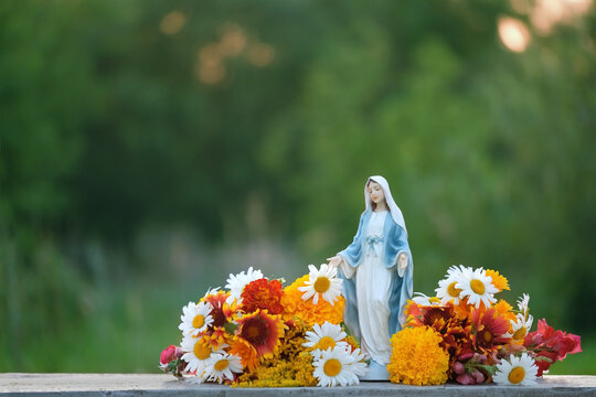 Figurine of Our lady, grace virgin Mary with flowers outdoor, natural background. Blessed Virgin Mary, Mother of God. Symbol of Hope, Love, pray, Faith of God. Religion ritual, church holiday