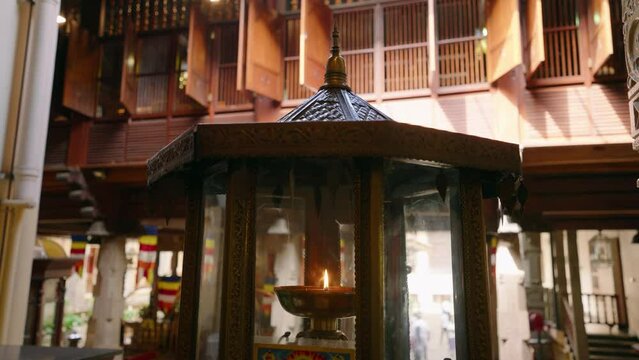 Traditional oil lamp burns at Buddhist temple, intricate design, warm glow amid historic architecture. Ambient flickers, serene prayer space, spiritual atmosphere in Kandy, ancient religious culture.