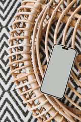 Mobile phone with blank screen on ornamental bamboo table and carpet. Mock up with copy space. Bohemian, coastal, organic modern and tropical style template. Flat lay, top view