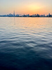 Naklejka premium city river at the sunset time, down town silhouette at the background, orange sky, water reflection 