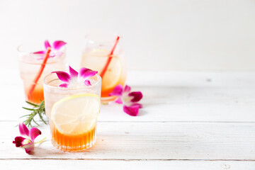 Glass of iced summer soda with lemon and pink orchid flower.