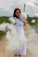pretty woman in a white dress and cute clouds with smoke with an umbrella