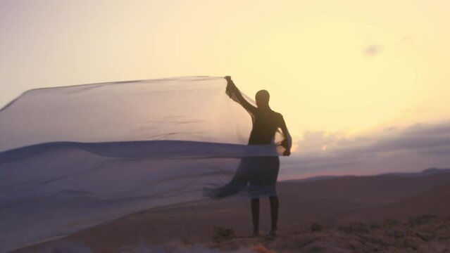 Model with shaved head holding a silk sheet in the wind in desert