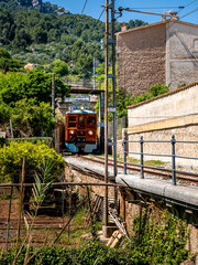 Leaving the last tunnel, the iconic Ferrocarril de Sóller train arrives on its historic route, winding through Sóller gardens, transporting tourists to the enchanting town, a real Mallorca experience.