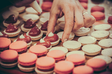Confectioner's hands filling macarons with pink ganache cream