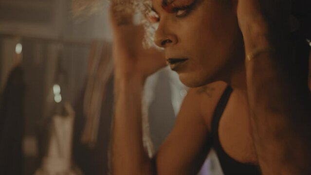Drag queen tucks in strands of hair into wig in dressing room
