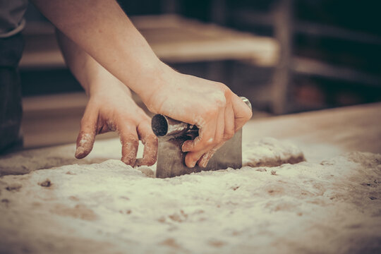 A female baker divides pieces of dough with a dough cutter. Vintage style with grain. - Powered by Adobe