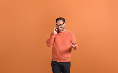 Positive young businessman discussing strategies over call on smart phone against orange background