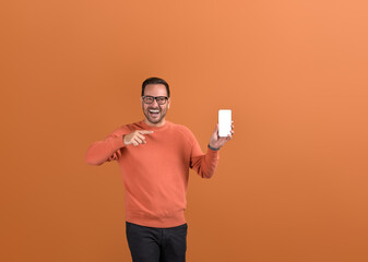 Cheerful young businessman pointing at smartphone and marketing new online apps on orange background