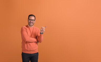 Portrait of cheerful young salesman pointing at copy space and advertising over orange background