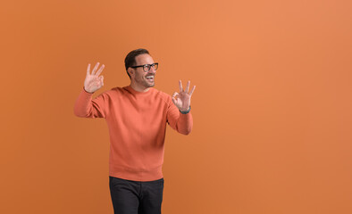 Male professional laughing and showing OK sign with both hands and looking away on orange background