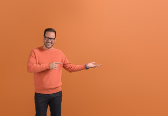 Portrait of smiling male promoter showing empty palm and marketing new product on orange background