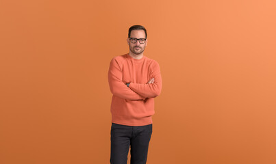 Portrait of serious young male entrepreneur with arms crossed posing on isolated orange background