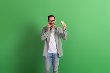 Portrait of happy businessman talking on mobile phone and showing credit card over green background