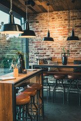 Seating area with bar tables and bar chairs in a modern cafe, industrial style with stone wall,...