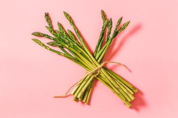 there is a bunch of green raw young asparagus on a pink background. healthy eating. spring vegetables. healthy food. vegan