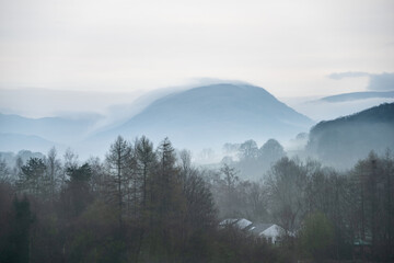 Stunning layered landscape image of misty Spring morning in Lake District looking towards distant misty peaks