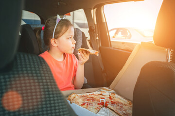 Portrait of little 5 YO girl eating just cooked Italian pizza sitting in child car seat on car back...