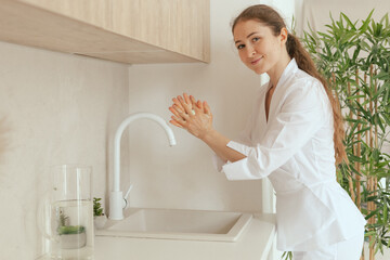 Close-up female gp physician doctor in white uniform washing hands on light background. Concept of...