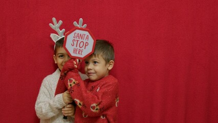Cute kids brothers hugging and showing santa stop here sign. Christmas celebration and happy family. High quality photo