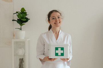 Medicine, healthcare and people concept - Friendly female gp physician doctor in white uniform is holding a first aid kit in the clinic office. Part of a series.