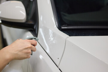 Person using black cloth to clean white cars hood, bumper, and tires