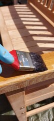 Painting a wooden bench outdoors with wood preservative using blue rubber gloves