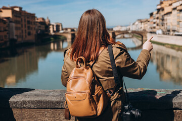Stylish Happy Young woman with camera enjoys beautiful view on famous Old bridge in Florence....