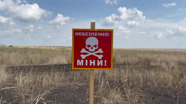 Red sign with markings about danger of finding mines on burnt and black agricultural field. Translation: Beware of mines. War Ukraine