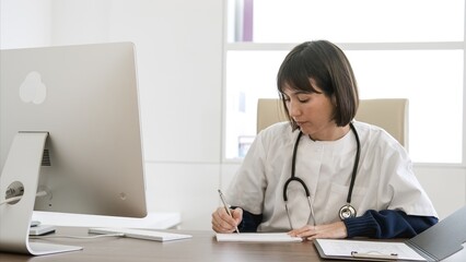 Confident female doctor writing prescription at desk in clinic
