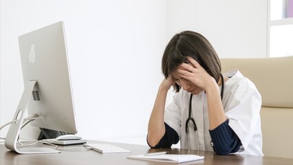 Stressed female doctor suffers from headache sitting at desk in clinic