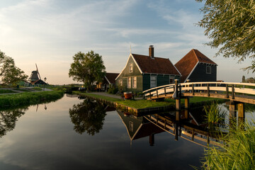 Obraz premium Beautiful village of Zaanse Schans in Netherlands at sunset with the wooden houses and the bridge reflected on the canal in a sunny day. Netherlands.