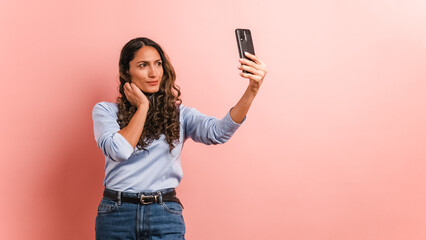 Naklejka premium Adult hispanic woman posing and smiling while taking selfie