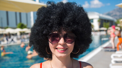 Summer day by the pool smiling woman with black curly hair., - obrazy, fototapety, plakaty