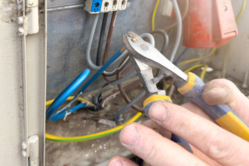 The electrician connects the wires in the shield. Hands of an electrician close-up with tongs cut...