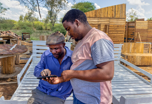 ngo social worker teaching a small business entrepreneur african american carpenter new skills, payments online for his outdoors wood furniture business on the side of the road